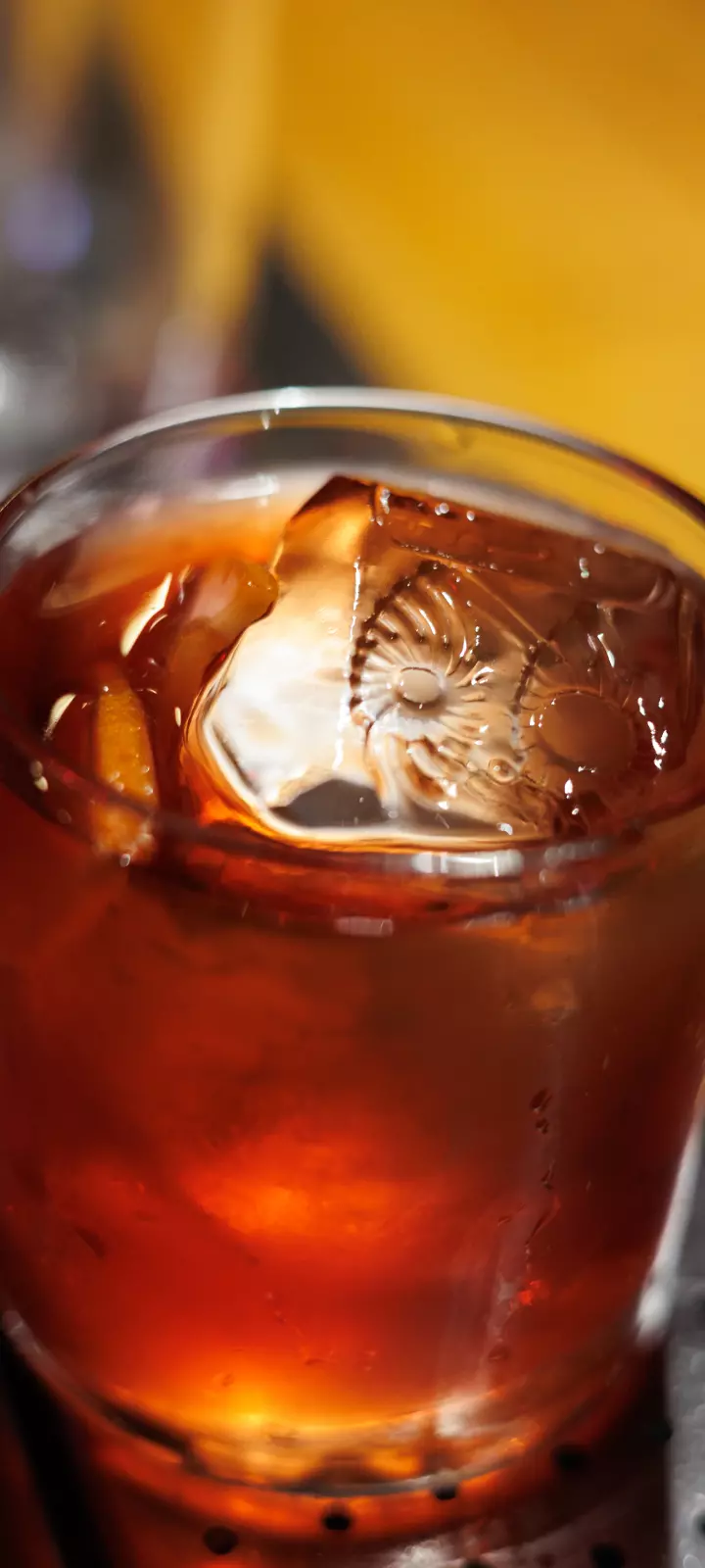 Foto bem próxima e detalhada de um drink do OIDĒ em copo de vidro. Na superfície um cubo de gelo com a gravação do símbolo do OIDĒ.